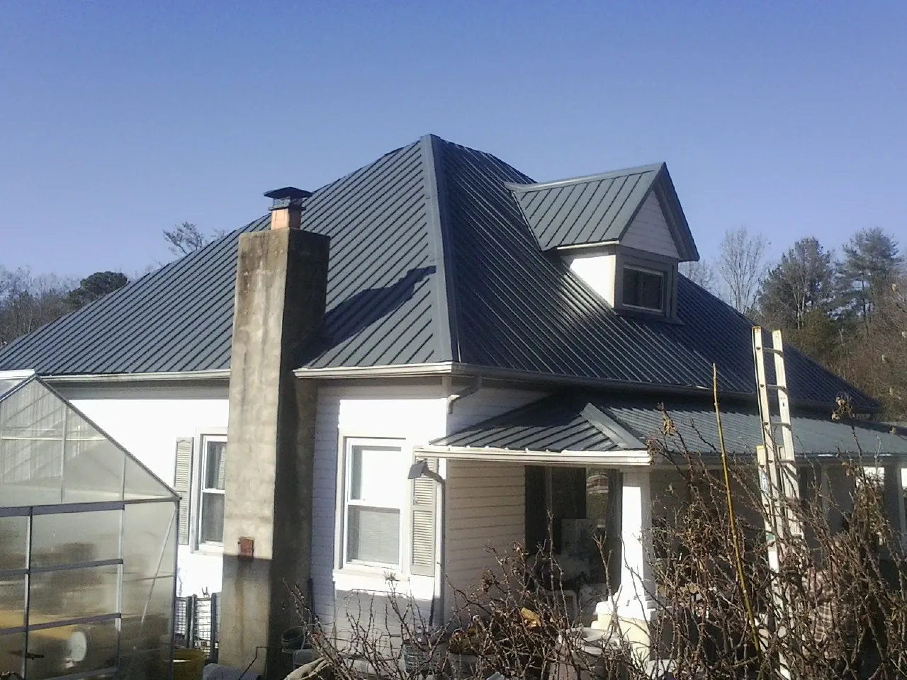 Dark blue standing seam metal roof on a white farmhouse with dormer — Slate & Tile Roof Repair by Roofing Brothers in New Marshfield