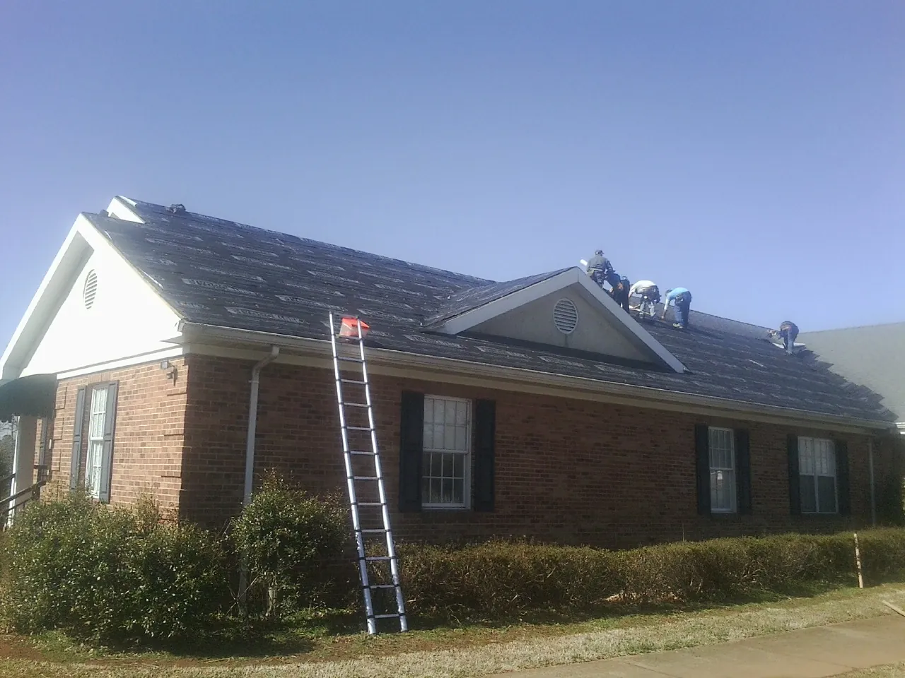 Crew tearing shingles off a brick ranch roof with a ladder set — Emergency Roof Repair work by our crew in New Marshfield