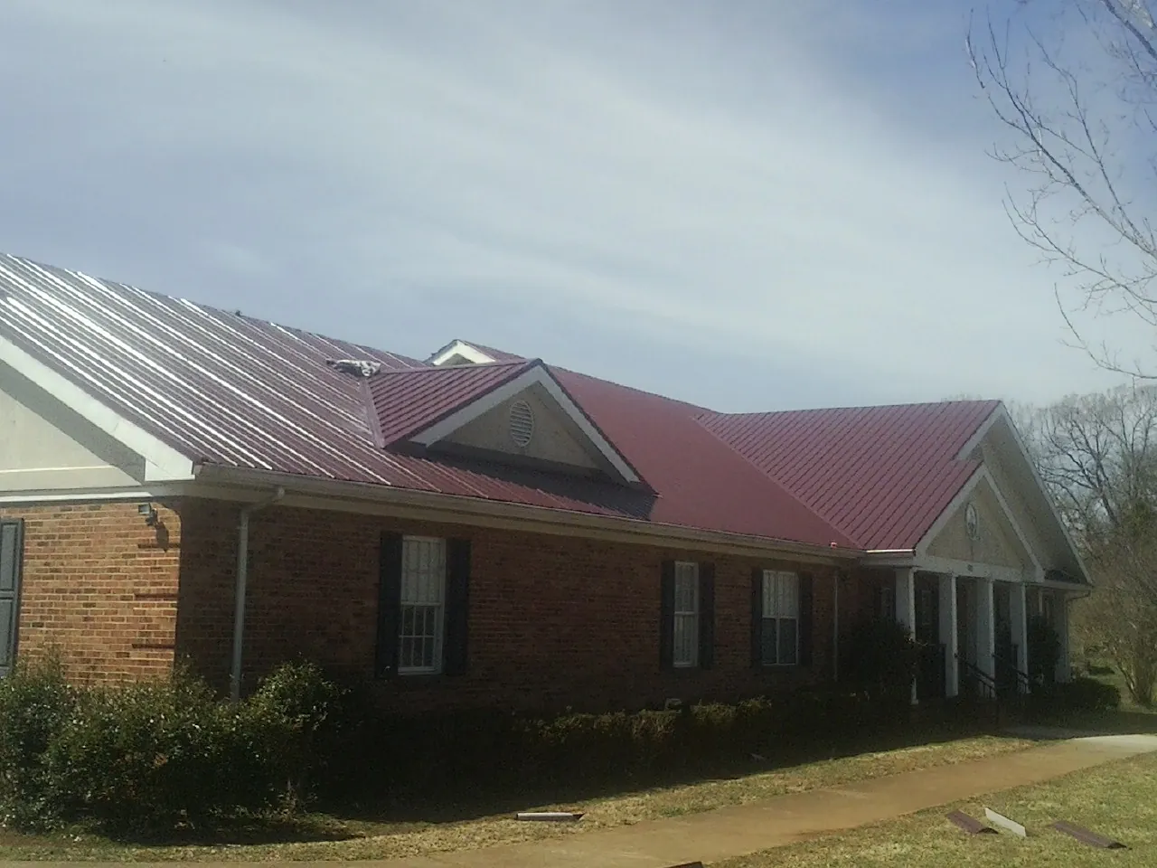 Red metal roof with gabled entries on a long brick building, from a Hail Damage Roof Repair job in New Marshfield