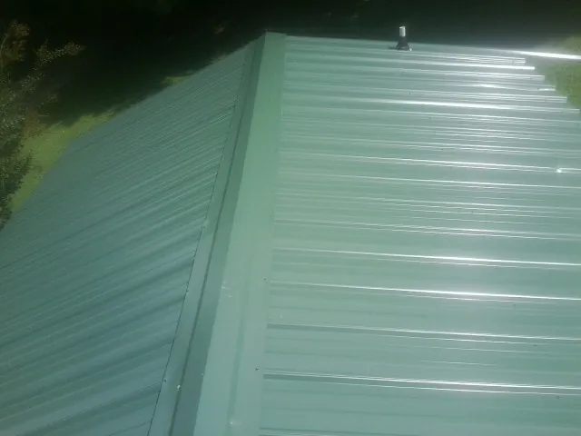 New green metal panels meeting at the ridge of a roof — Flat Roof Repair work by our crew in New Marshfield