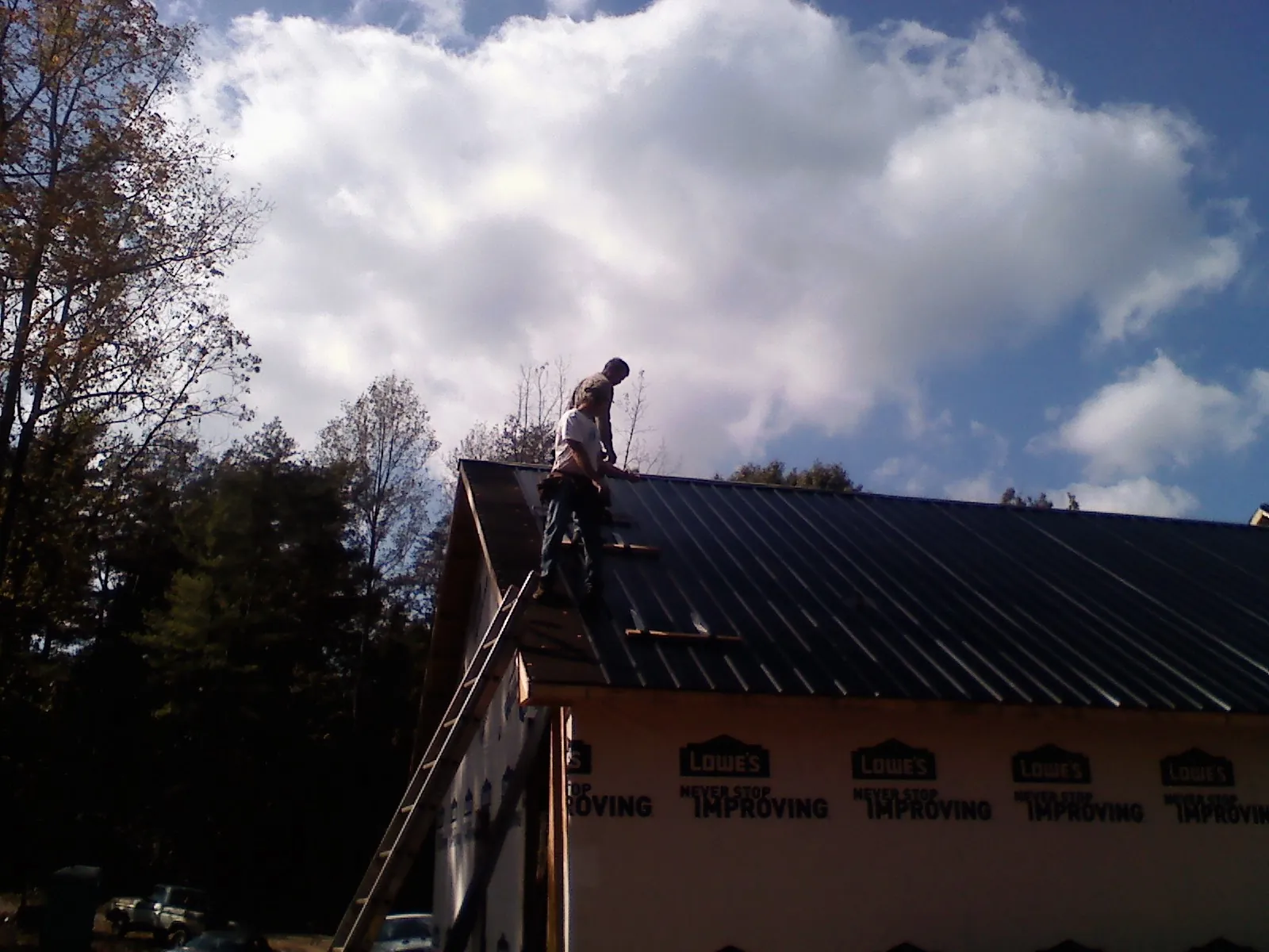 Roofer fastening dark metal panels high against a cloudy sky, from a Roof Inspection job in New Marshfield