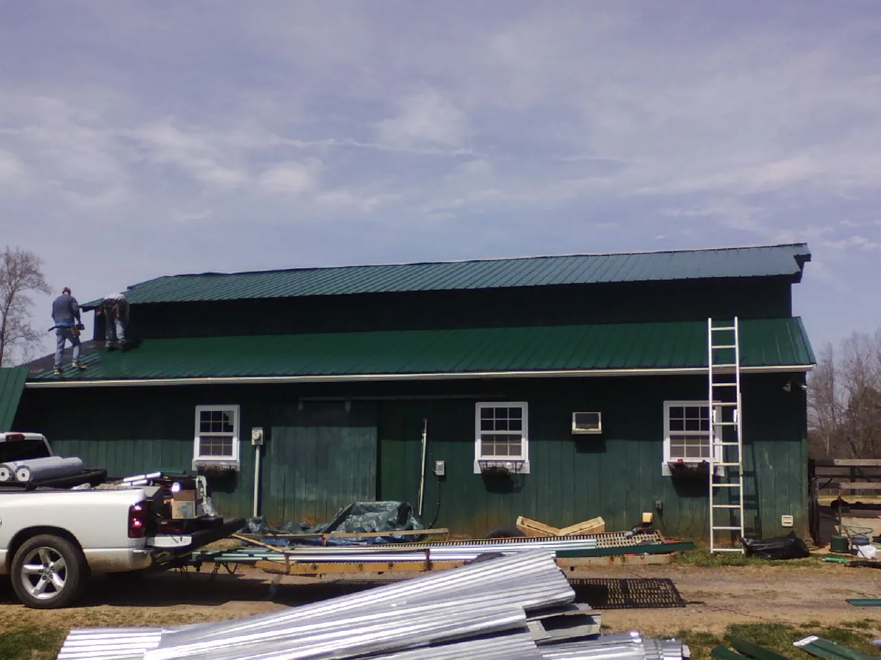 Crew installing green metal roofing on a large green barn in New Marshfield