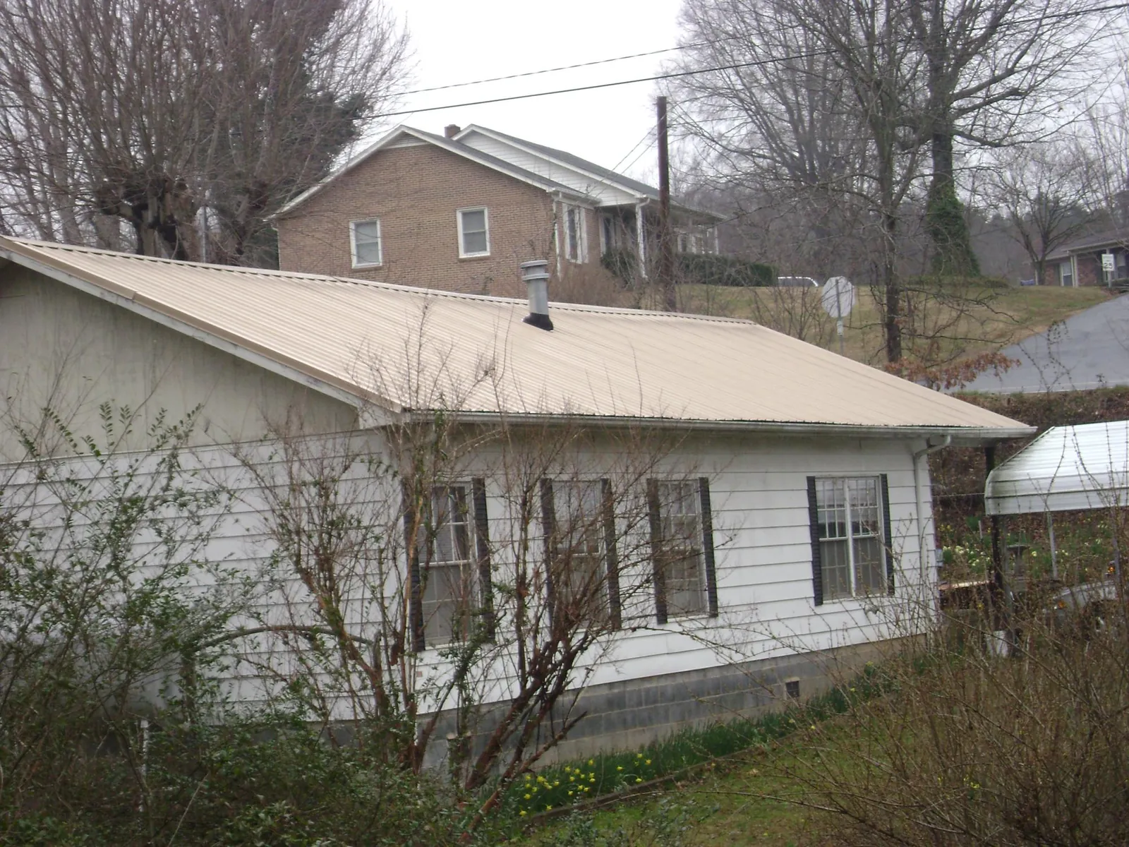 Tan metal roof on a white sided house set into a hillside — Commercial Roofing by Roofing Brothers in New Marshfield